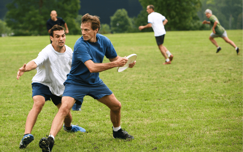 Players throwing and catching frisbees on a field, with goal posts in the background